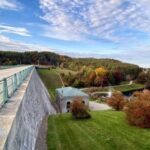 View from a reservoir dam overlooking wooded hills, water, and parkland