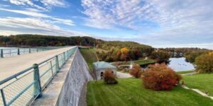 View from a reservoir dam overlooking wooded hills, water, and parkland