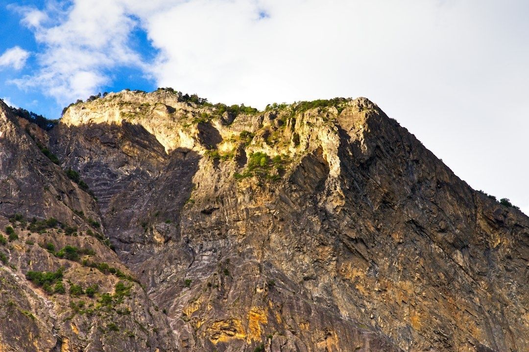 Sunlit, rugged basalt cliff ridge beneath a partly cloudy blue sky