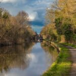 Canal towpath with a narrowboat, trees, and a stone bridge