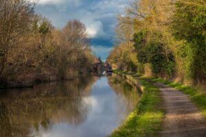 Canal towpath with a narrowboat, trees, and a stone bridge