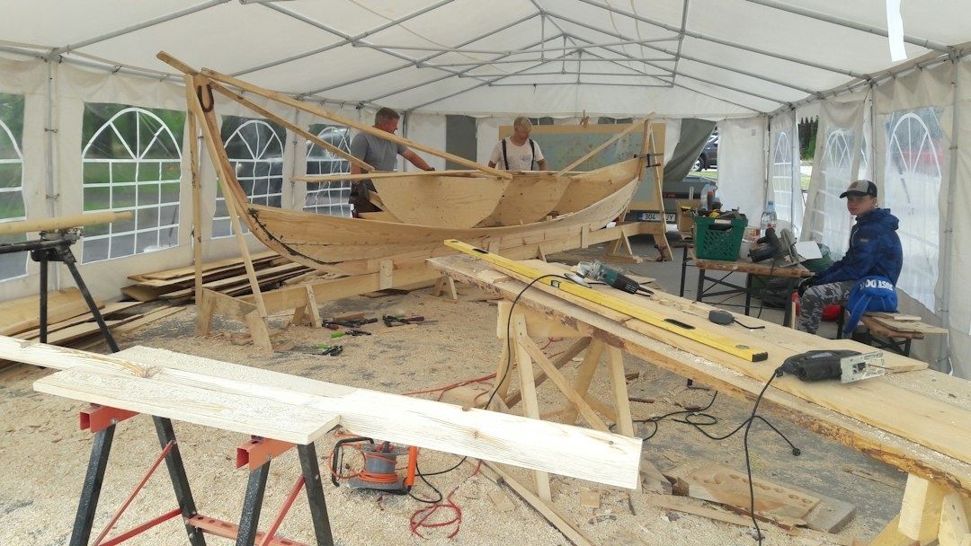 Shipwrights shaping a wooden boat inside a temporary workshop tent